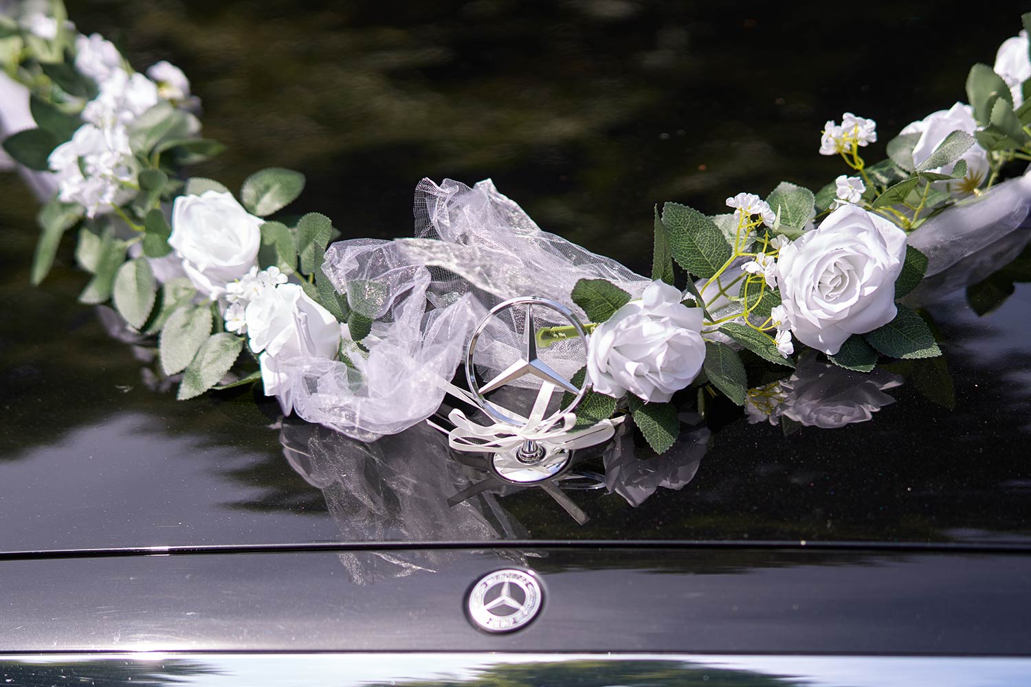 Detail der Hochzeitsdekoration am Mercedes – weiße Rosen, Tüll und Mercedes-Stern auf der Motorhaube | Autovermietung Arndt