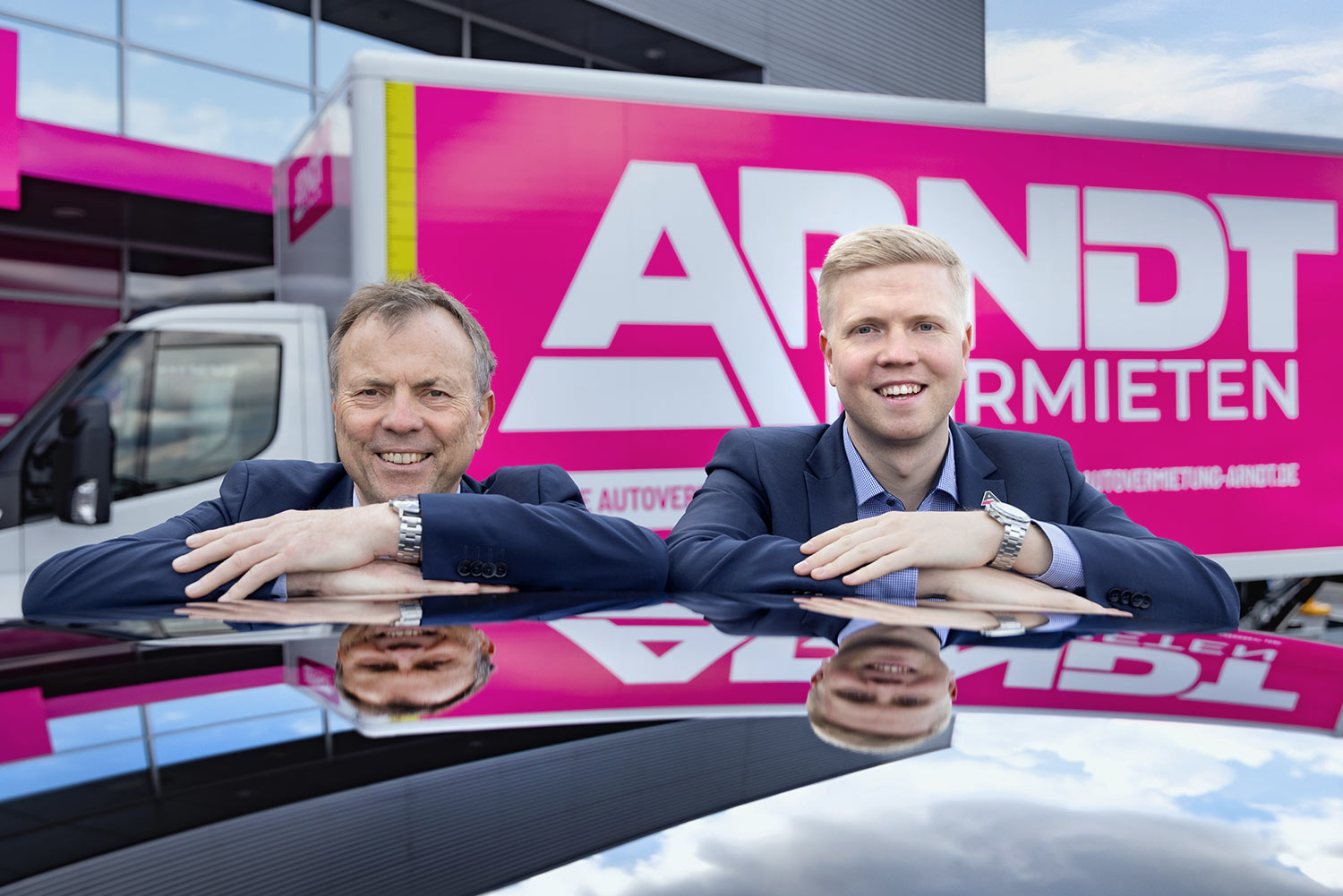 Die Geschäftsführer Matthias und Moritz Arndt lehnen lächelnd an einem Fahrzeug | Autovermietung Arndt